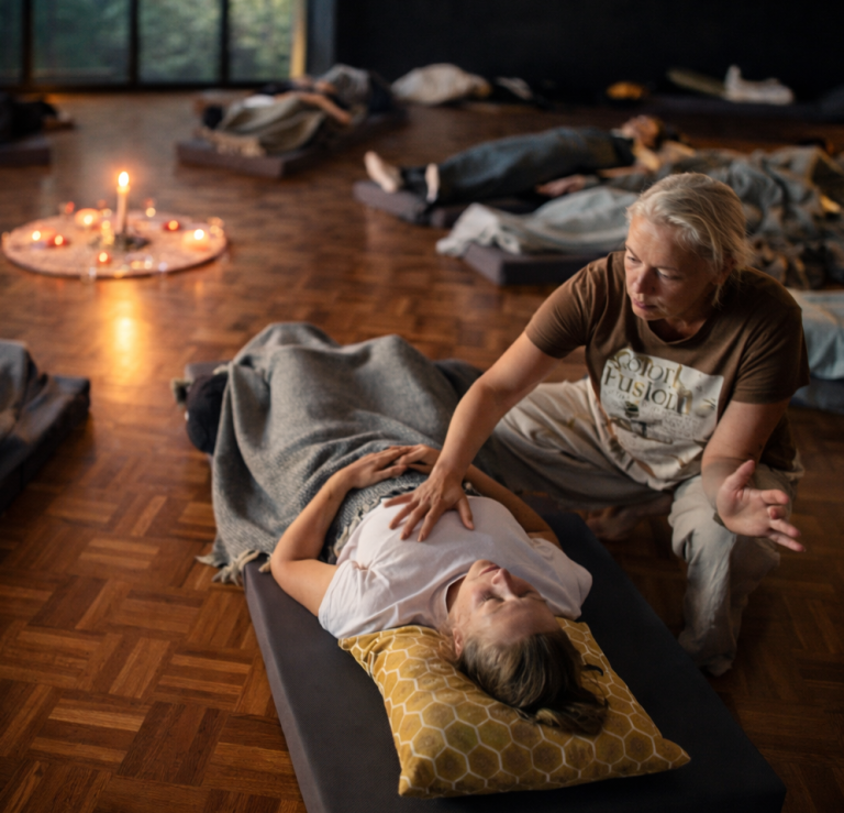 Een vrouw biedt ondersteuning aan een liggende deelnemer in een rustige, verlichte ruimte tijdens een ademreis