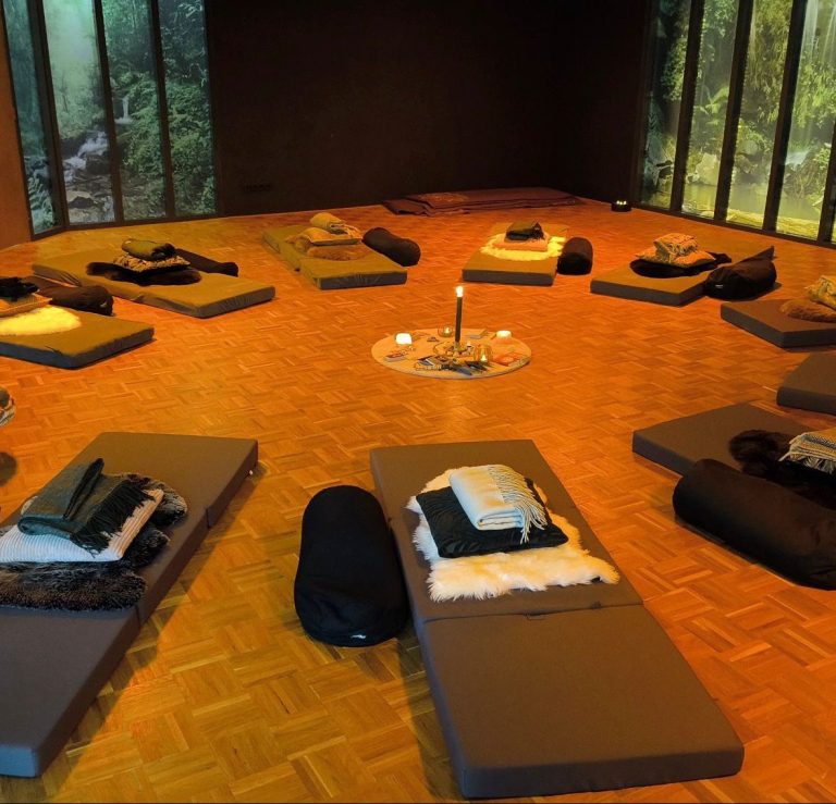 Meditatieruimte met matten, kussens, dekens en een centrale kaarsverlichting.